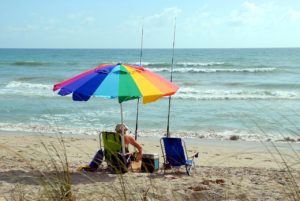 Man sitting on the beach in a beach chair with an umbrella and two fishing poles